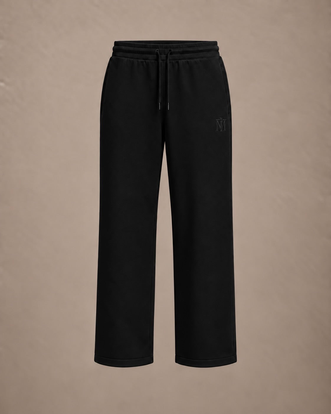 Black wide-leg sweatpants with an elastic drawstring waist and a subtle tonal embroidered logo on the left thigh, shown against a solid beige background.